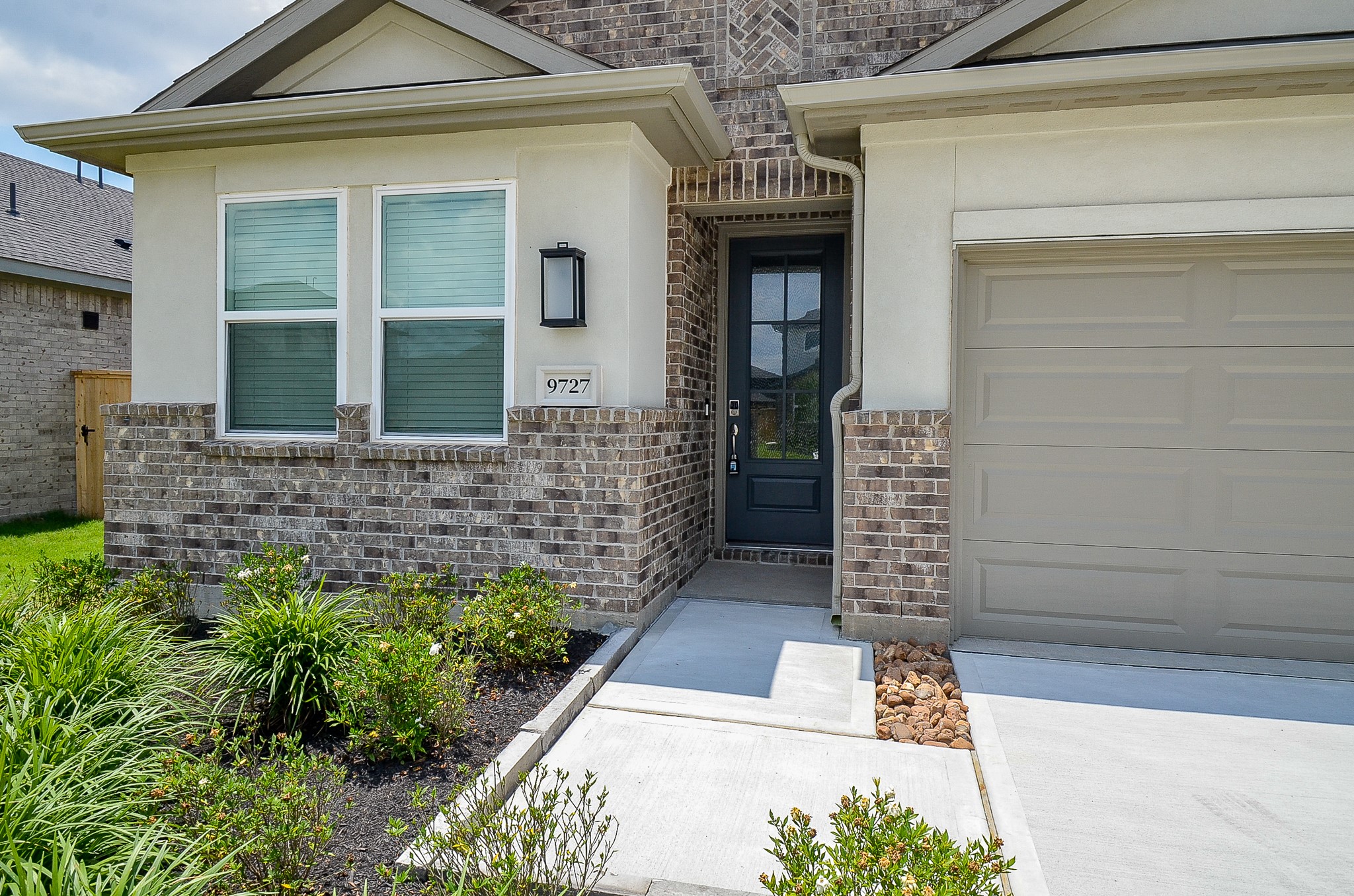 9727 Rialto Hts Drive Cypress, TX 77433 - Photo 4 of 37 This photo shows the entrance of a modern home with a mix of brick and light-colored siding. It features a welcoming front door, adjacent garage, and a well-maintained garden with shrubs and plants.