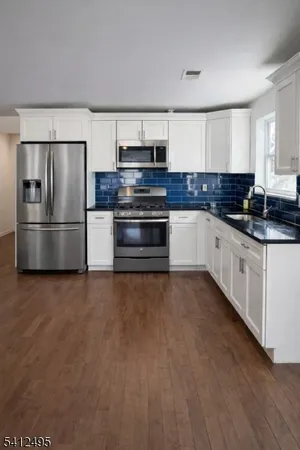 a living room with stainless steel appliances kitchen island granite countertop a stove a sink dishwasher and white cabinets with wooden floor