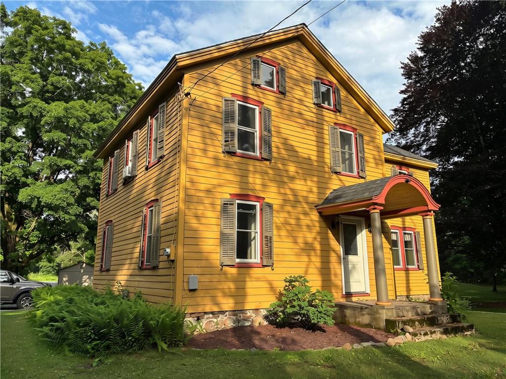 A charming yellow home with a welcoming arched entryway is nestled among verdant trees.