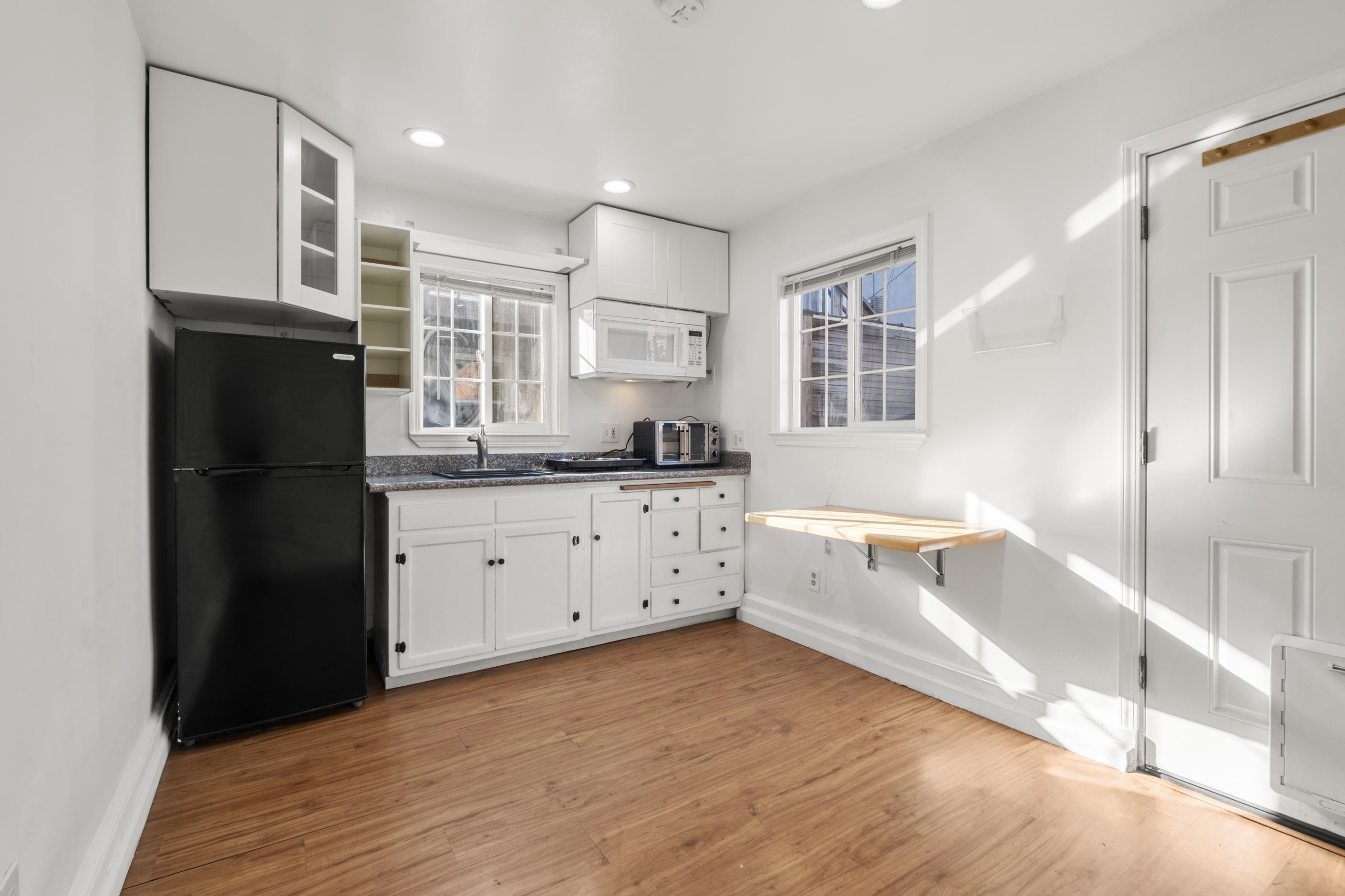 1039 Channing Way Berkeley, CA 94710 - Photo 9 of 25 Kitchen featuring white cabinets, freestanding refrigerator, light wood-style flooring, glass insert cabinets, and white microwave