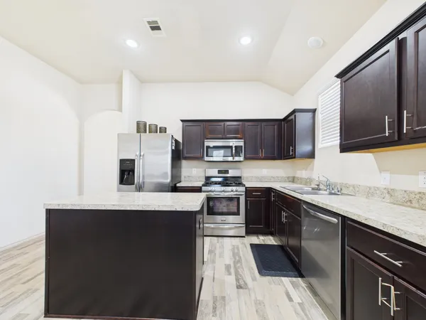 a large kitchen with stainless steel appliances kitchen island granite countertop a sink and stove top oven with wooden floor