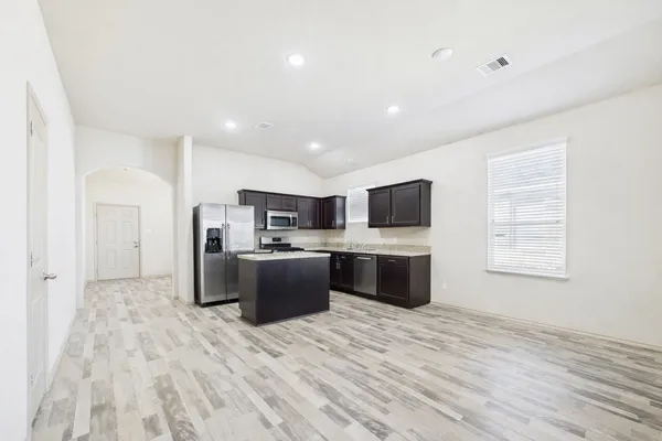 a large white kitchen with stainless steel appliances kitchen island a sink dishwasher a refrigerator and a stove with wooden floor