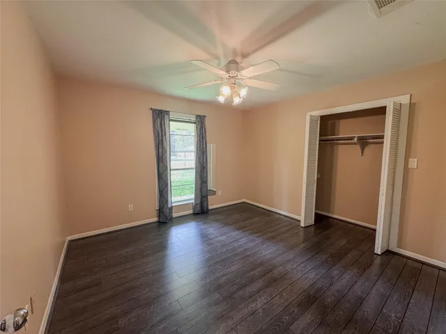 an empty room with wooden floor closet fan and windows