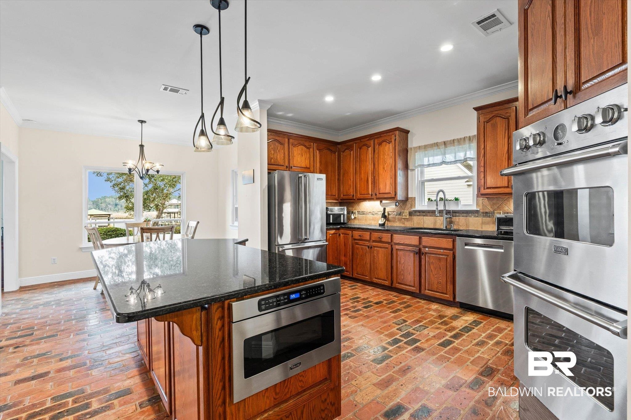 4851 Audubon Drive Mobile, AL 36619 - Photo 9 of 46 Kitchen featuring brown cabinetry, dark stone counters, stainless steel appliances, a center island, and backsplash