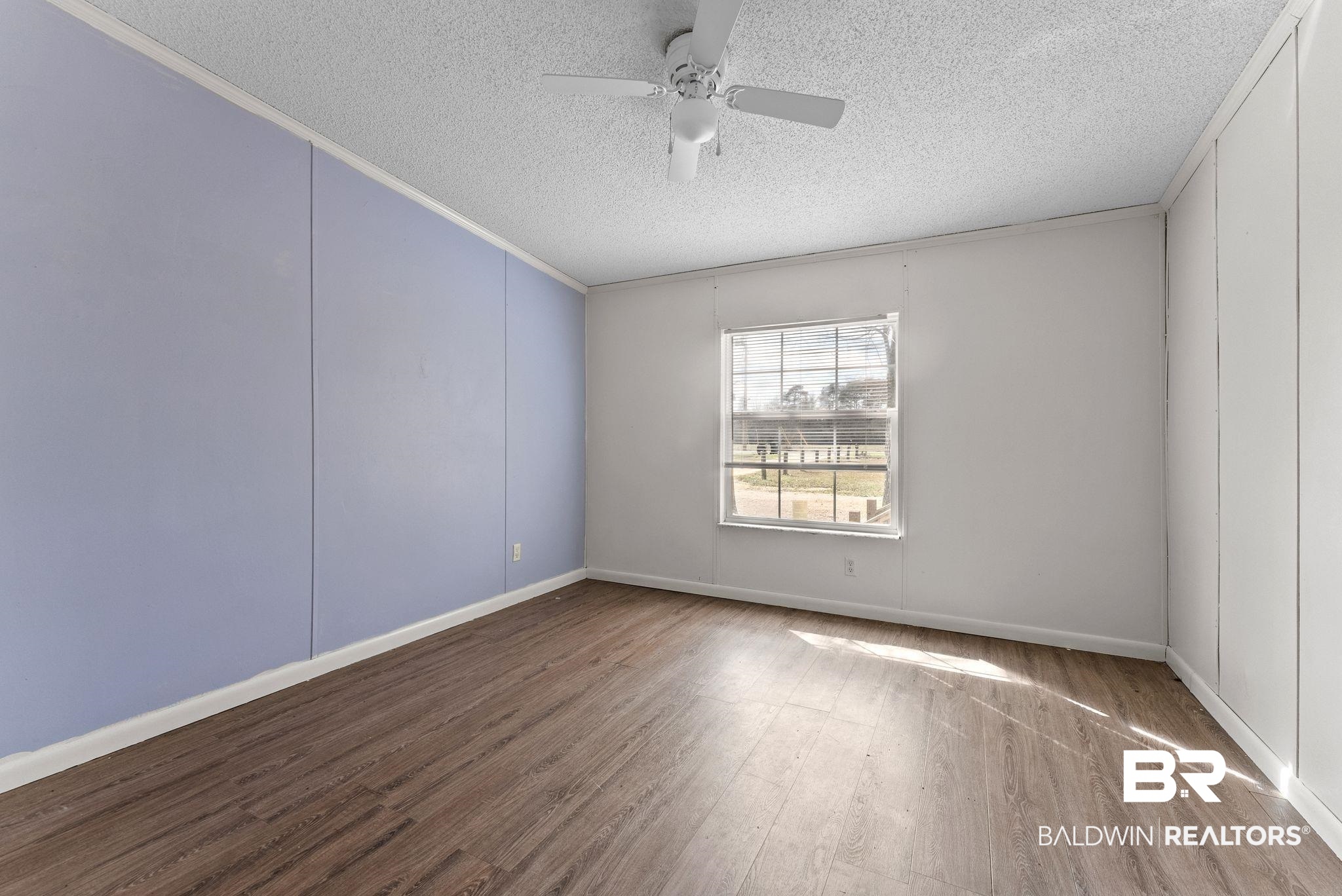34904 Pine Road South Stapleton, AL 36578 - Photo 18 of 42 Empty room with a textured ceiling, wood finished floors, ceiling fan, ornamental molding, and a decorative wall
