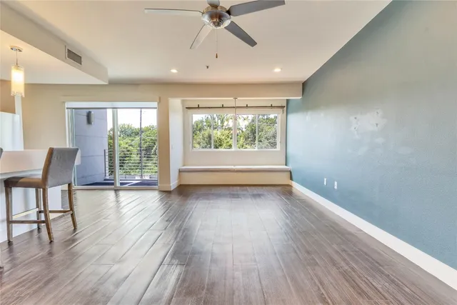 an empty room with wooden floor fan and windows