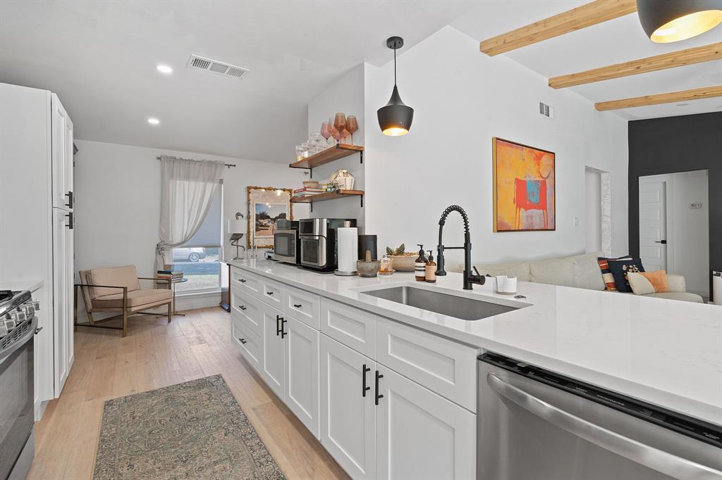 4902 Carsonhill Drive Austin, TX 78723 - Photo 11 of 19 Kitchen featuring white cabinetry, stainless steel appliances, decorative light fixtures, light stone countertops, and light wood-style floors