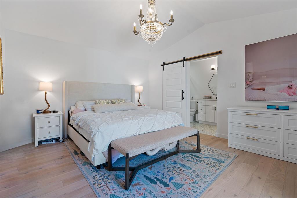 4902 Carsonhill Drive Austin, TX 78723 - Photo 13 of 19 Bedroom featuring a barn door, light wood-style floors, a chandelier, vaulted ceiling, and connected bathroom