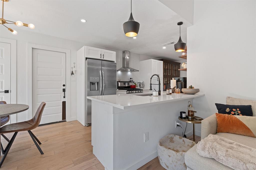 4902 Carsonhill Drive Austin, TX 78723 - Photo 8 of 19 Kitchen featuring stainless steel appliances, light wood-style flooring, white cabinetry, wall chimney range hood, and a peninsula