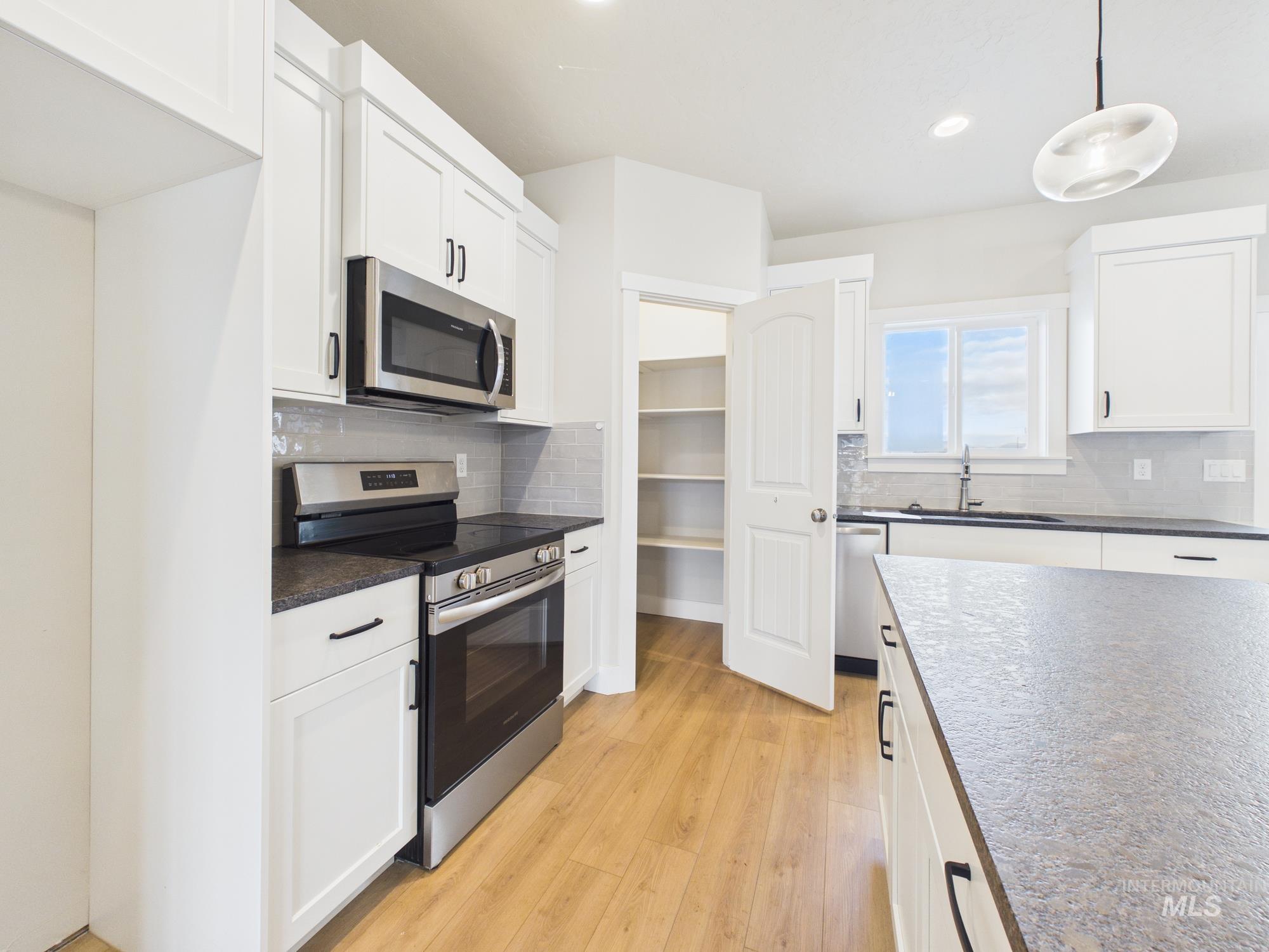 1545 Trail Way Weiser, ID 83672 - Photo 10 of 50 Kitchen with stainless steel appliances, light wood-style floors, white cabinets, hanging light fixtures, and decorative backsplash