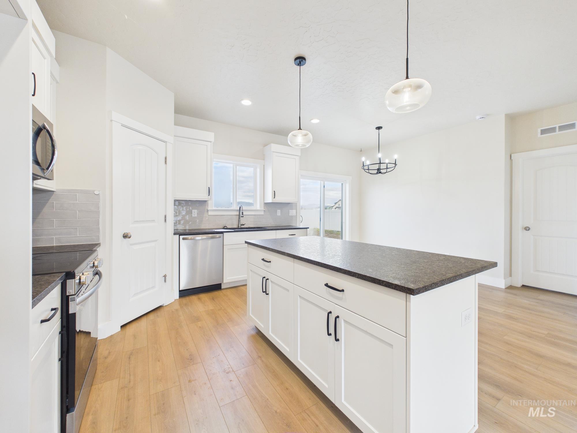 1545 Trail Way Weiser, ID 83672 - Photo 16 of 50 Kitchen with stainless steel appliances, dark countertops, white cabinets, light wood-style floors, and a kitchen island