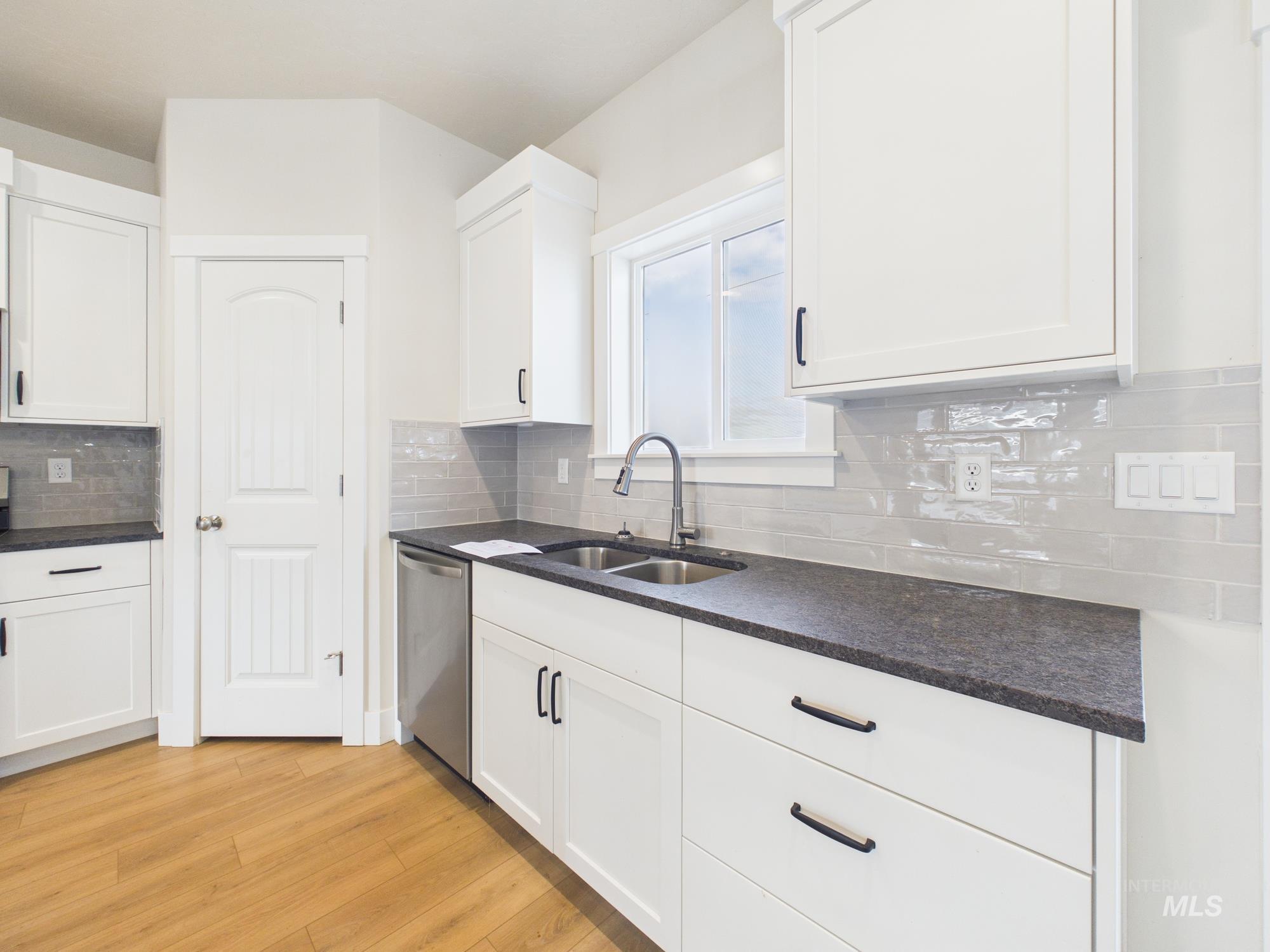 1545 Trail Way Weiser, ID 83672 - Photo 9 of 50 Kitchen with white cabinets, light wood finished floors, dishwasher, decorative backsplash, and dark stone counters
