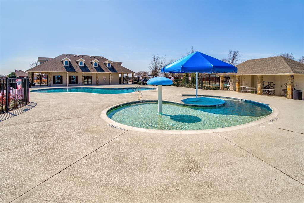 4305 Ridgewood Road Melissa, TX 75454 - Photo 24 of 26 Community pool area featuring a large swimming pool, a separate shallow splash pad with a blue shade umbrella, a stone-accented pool house with a covered patio, and a distant clubhouse building with multiple dormer windows