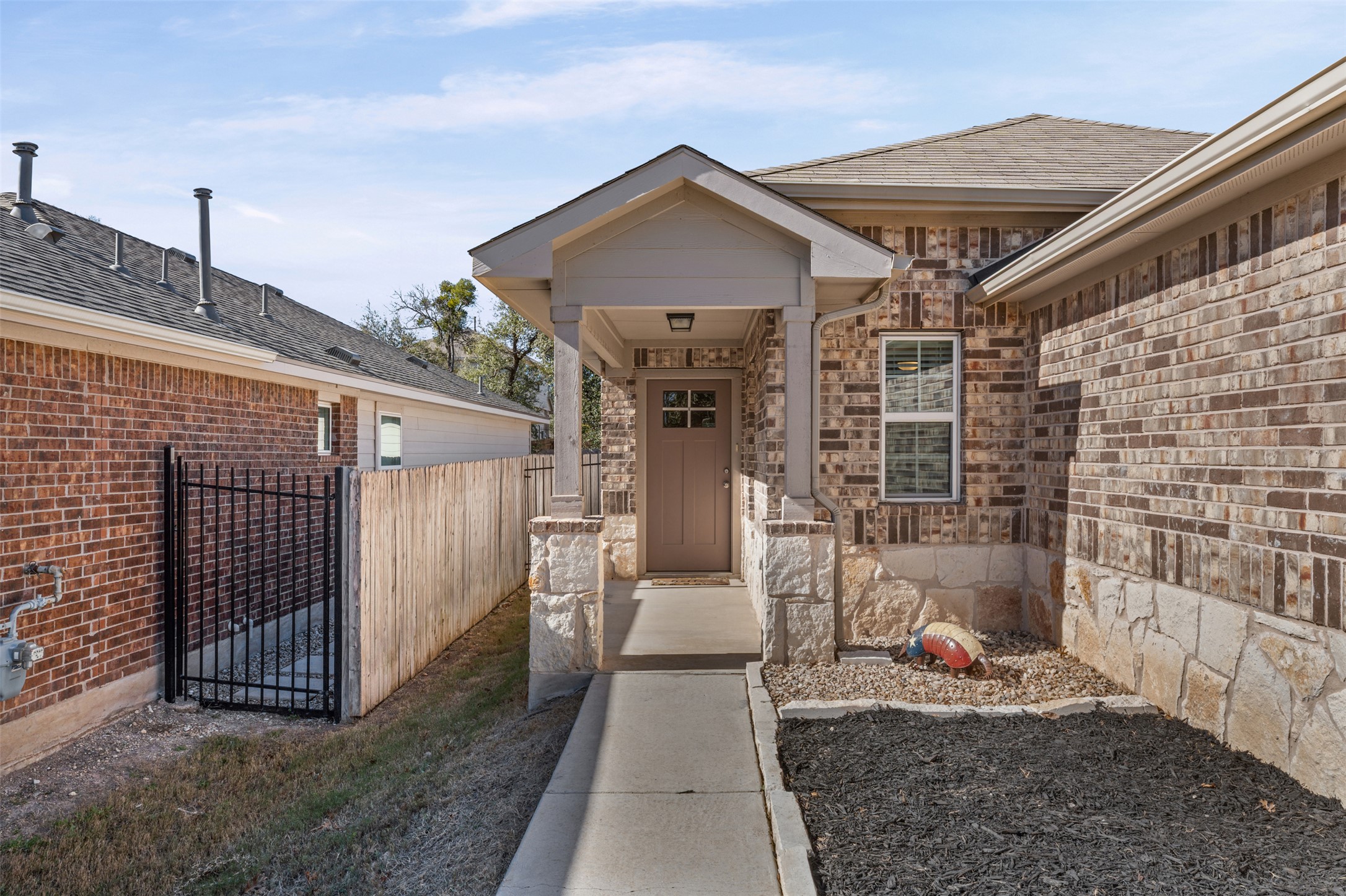 View of exterior entry featuring a gate, brick siding, roof with shingles, and stone siding