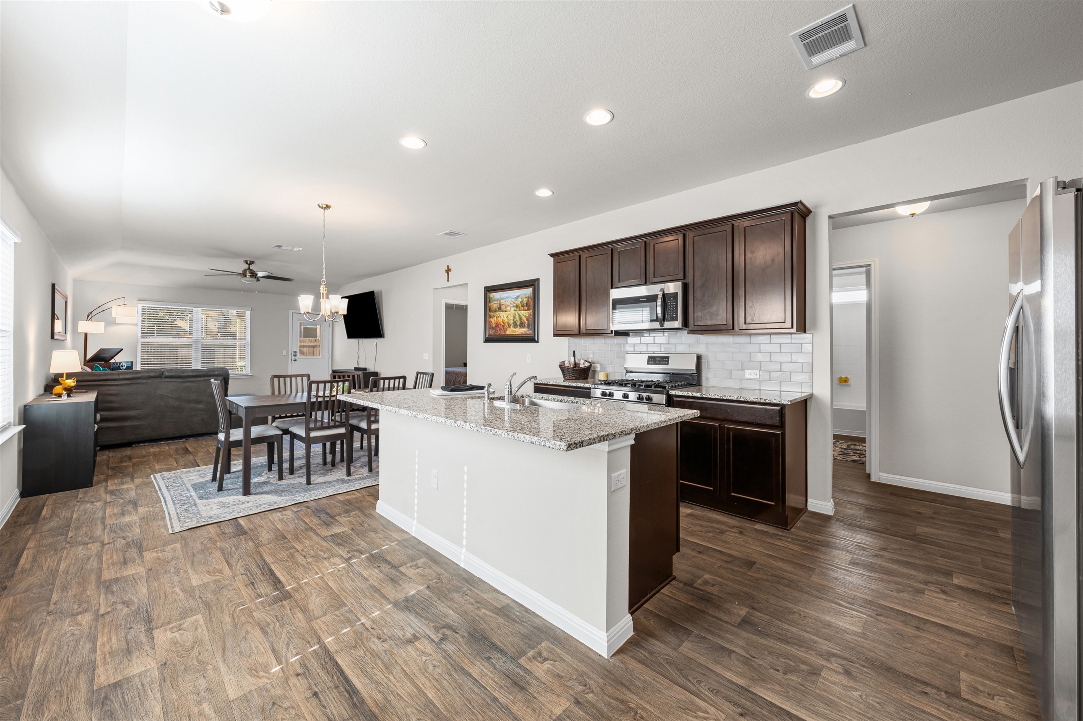 132 Dunlin Lane Leander, TX 78641 - Photo 4 of 34 Kitchen featuring light stone countertops, dark brown cabinets, pendant lighting, stainless steel appliances, and an island with sink