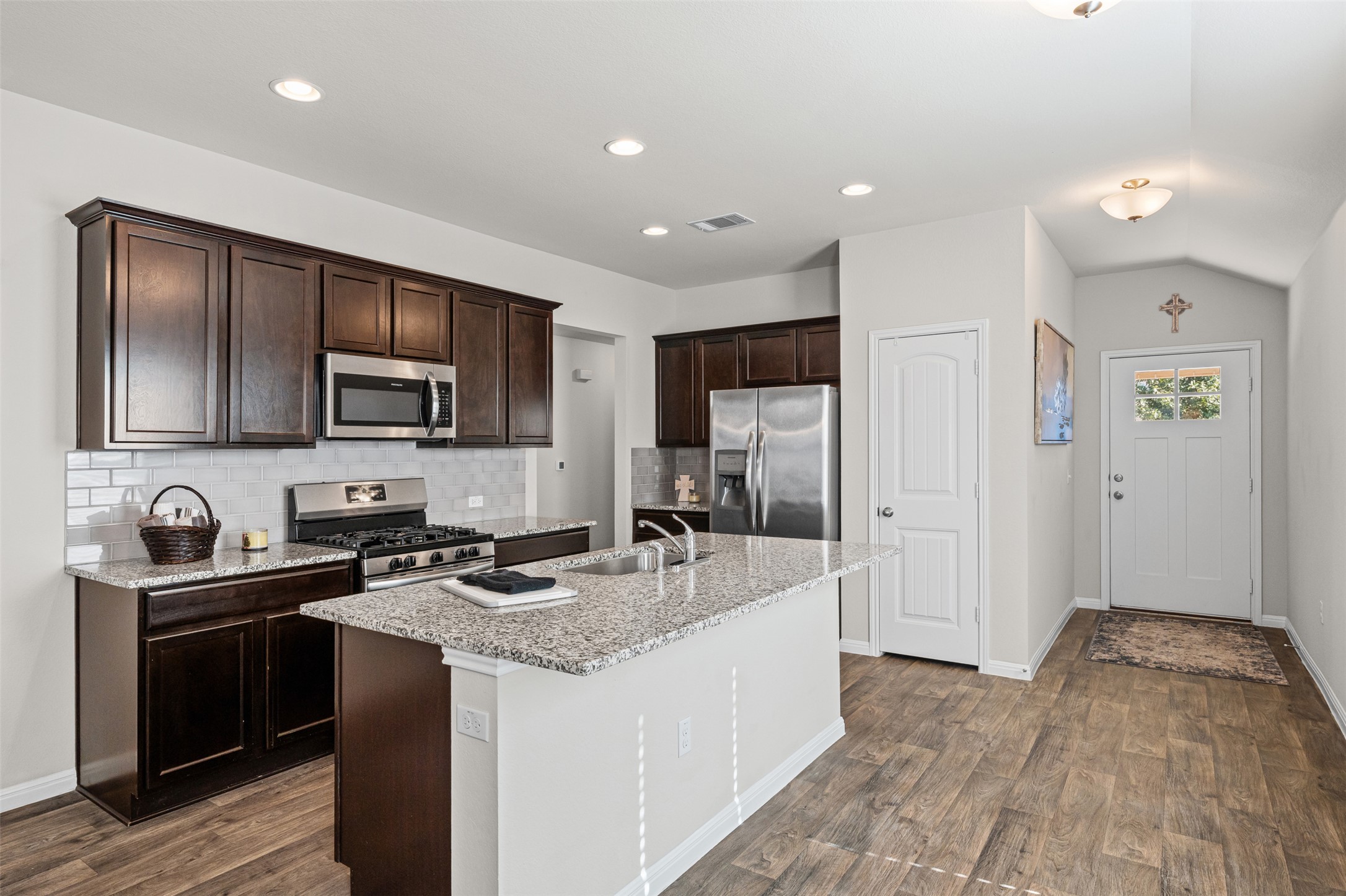 132 Dunlin Lane Leander, TX 78641 - Photo 6 of 34 Kitchen with dark brown cabinets, appliances with stainless steel finishes, light stone counters, vaulted ceiling, and an island with sink