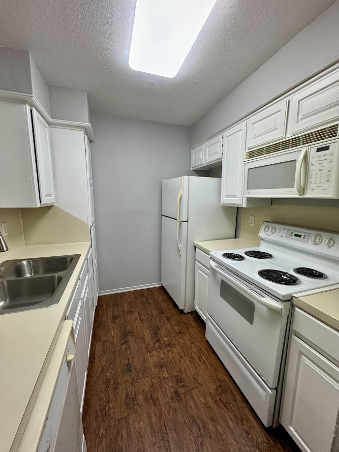 1305 West Villa Maria Road, Unit C107 Bryan, TX 77801 - Photo 10 of 19 Kitchen featuring white appliances, white cabinets, dark wood finished floors, light countertops, and a textured ceiling
