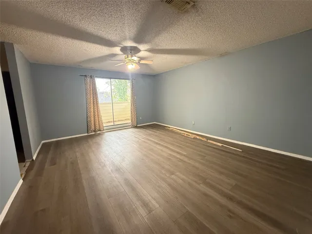 an empty room with wooden floor fan and windows