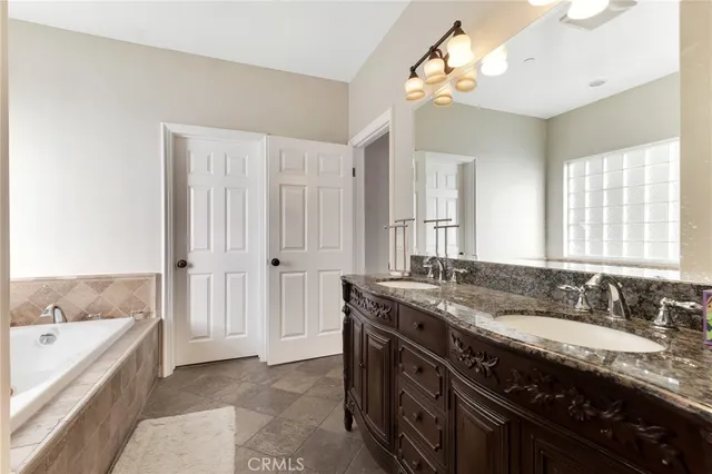 a spacious bathroom with a granite countertop double vanity sink a mirror and a bathtub