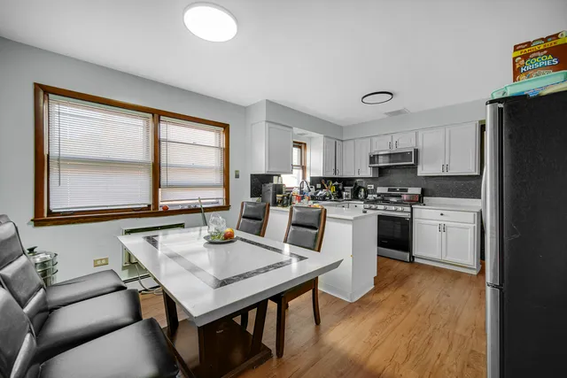 a kitchen with stainless steel appliances granite countertop a stove a refrigerator a sink a dining table and chairs with wooden floor