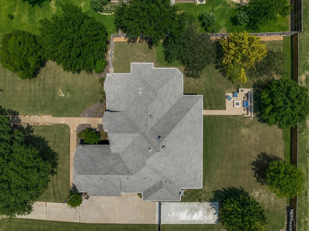 229 Arbor Lane Haslet, TX 76052 - Photo 28 of 34 Expansive property featuring a grey shingle roof, paved driveway, multiple mature trees, and a backyard patio with a built-in fire pit