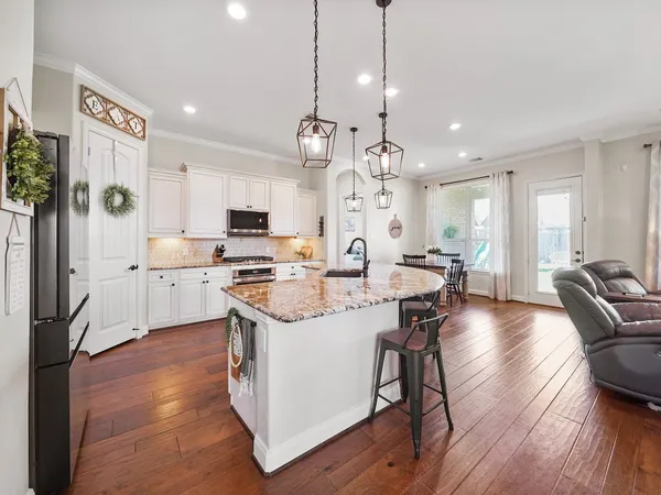a large kitchen with stainless steel appliances kitchen island granite countertop a stove a sink a refrigerator and a dining table with wooden floor