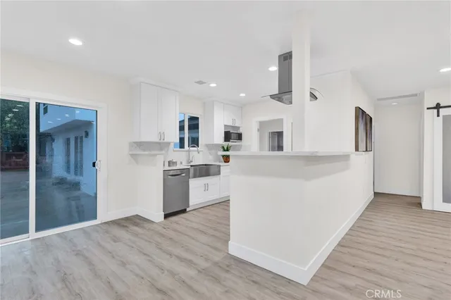 a living room with stainless steel appliances kitchen island wooden floors and white walls