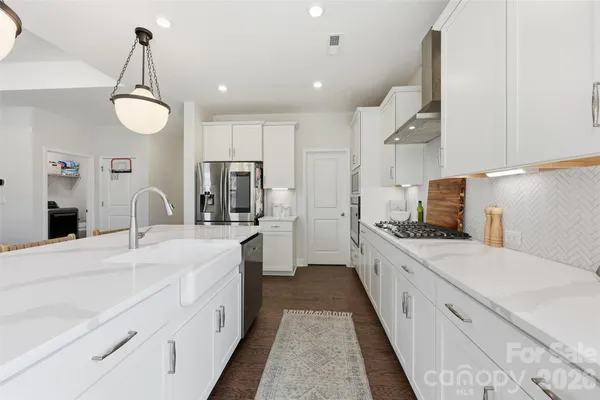 a large white kitchen with kitchen island a sink stainless steel appliances and cabinets