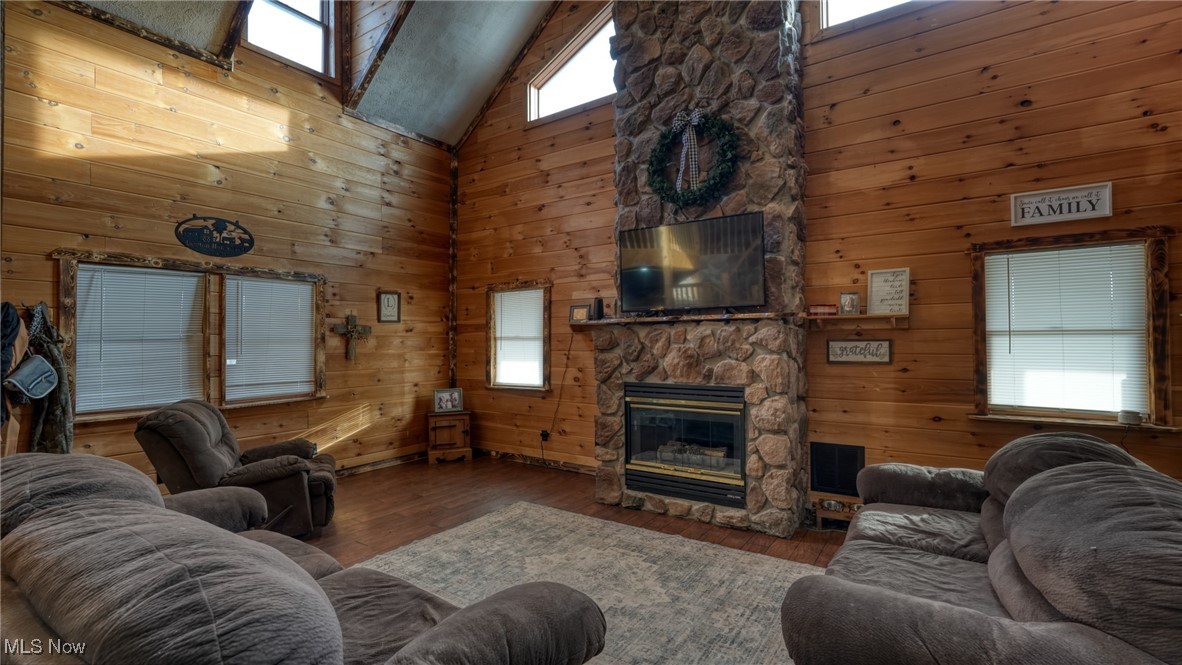 8498 Euga Road Newcomerstown, OH 43832 - Photo 7 of 49 Living room with high vaulted ceiling, wood walls, a stone fireplace, and wood-type flooring