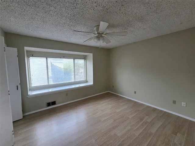 an empty room with wooden floor chandelier fan and windows