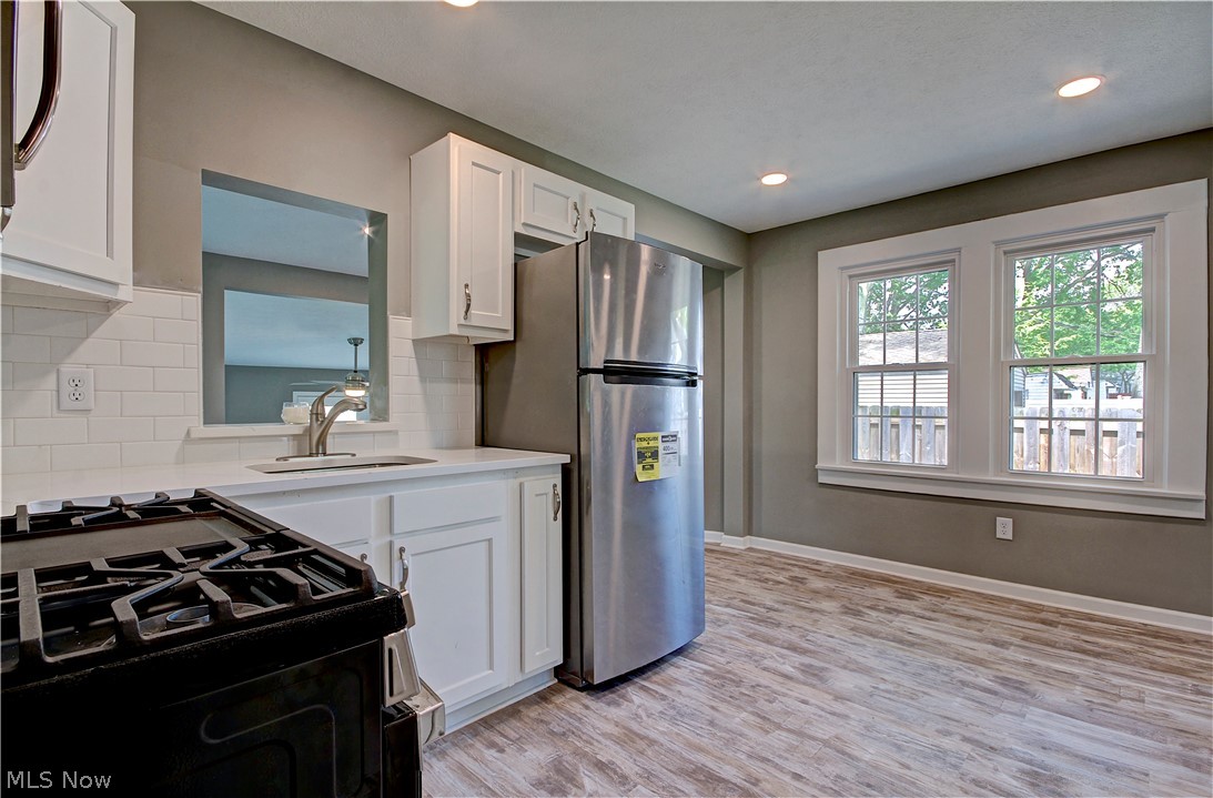 14507 Glencliffe Road Cleveland, OH 44111 - Photo 13 of 31 Kitchen with light hardwood / wood-style floors, white cabinets, backsplash, stainless steel refrigerator, and gas range