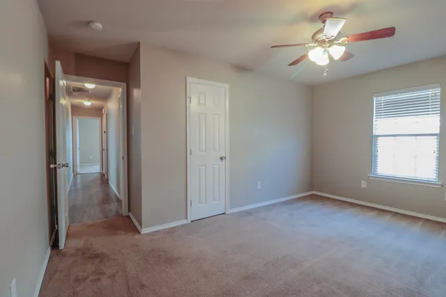 an empty room with chandelier fan and windows