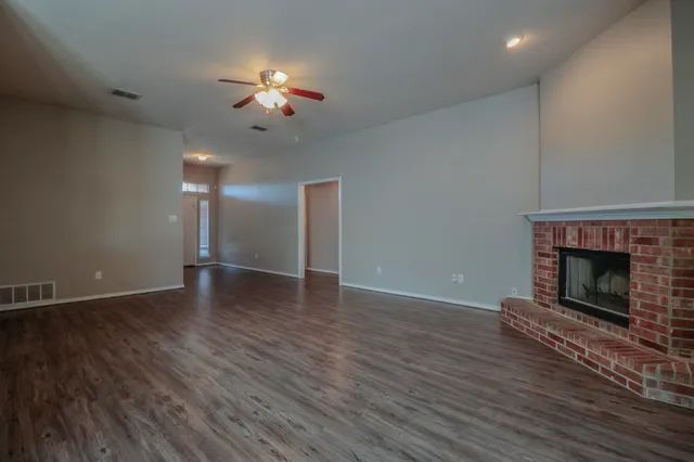 a view of an empty room with wooden floor fireplace and a window