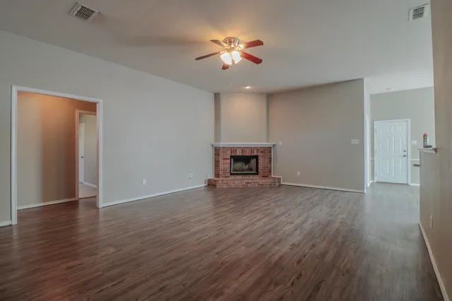 a view of an empty room with wooden floor and a ceiling fan