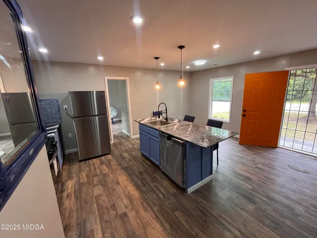 a kitchen with stainless steel appliances granite countertop a refrigerator a sink dishwasher a oven and a dining table with wooden floor