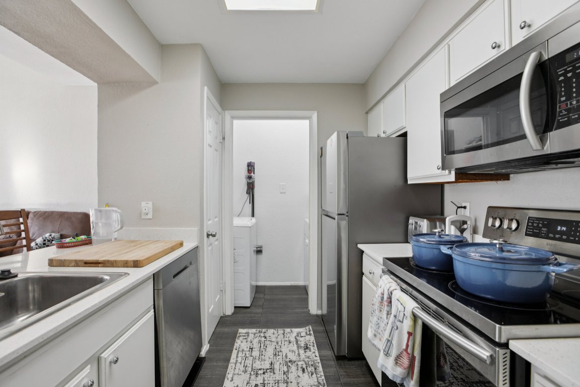 807 West 25th Street, Unit 302 Austin, TX 78705 - Photo 3 of 18 Kitchen featuring appliances with stainless steel finishes, white cabinets, light countertops, and dark wood-style floors