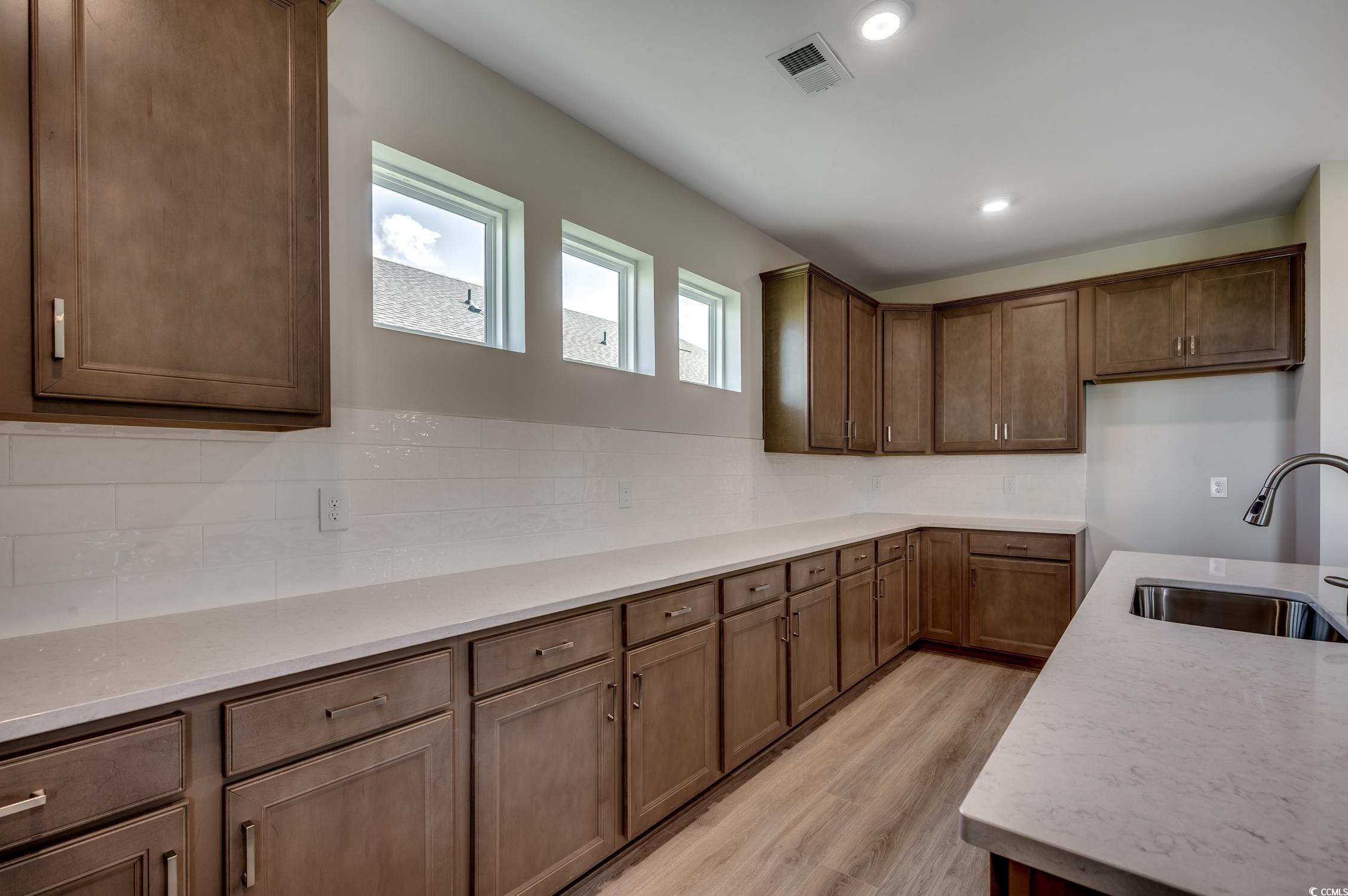 439 Kapalua Loop Little River, SC 29566 - Photo 13 of 36 Kitchen featuring light wood-style flooring, decorative backsplash, light stone countertops, recessed lighting, and brown cabinets