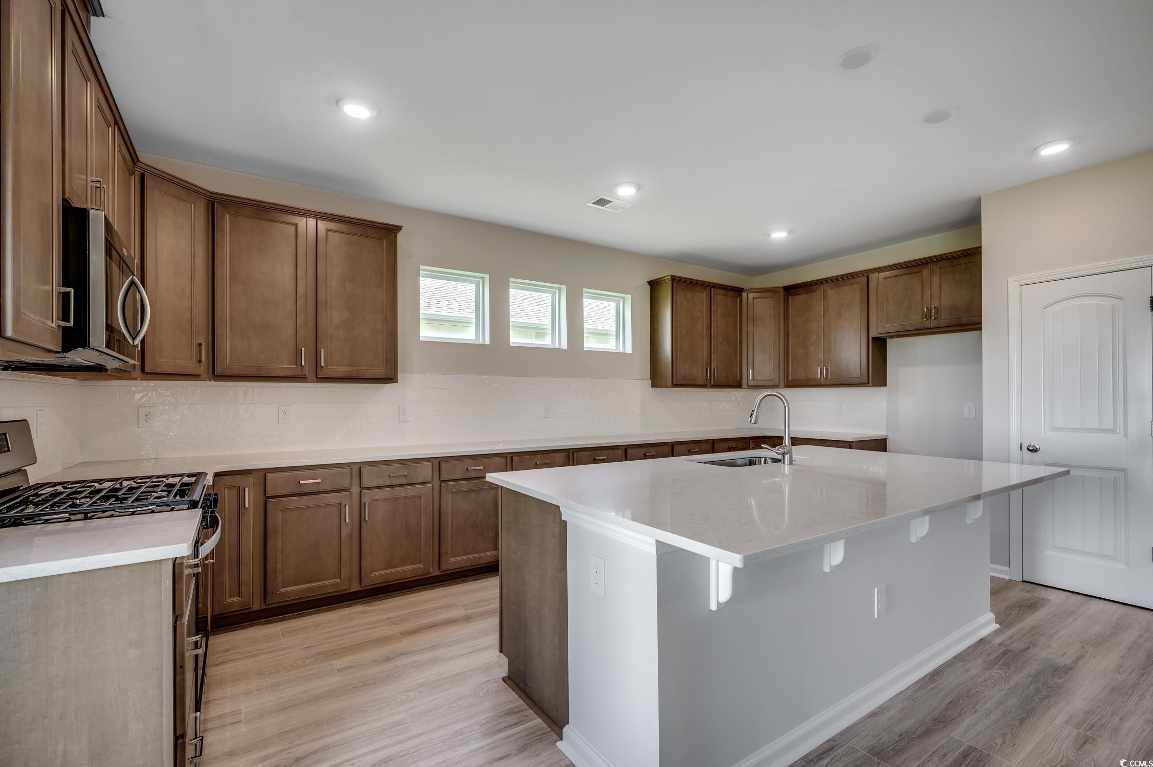 439 Kapalua Loop Little River, SC 29566 - Photo 15 of 36 Kitchen featuring stainless steel appliances, tasteful backsplash, an island with sink, light stone countertops, and a kitchen breakfast bar