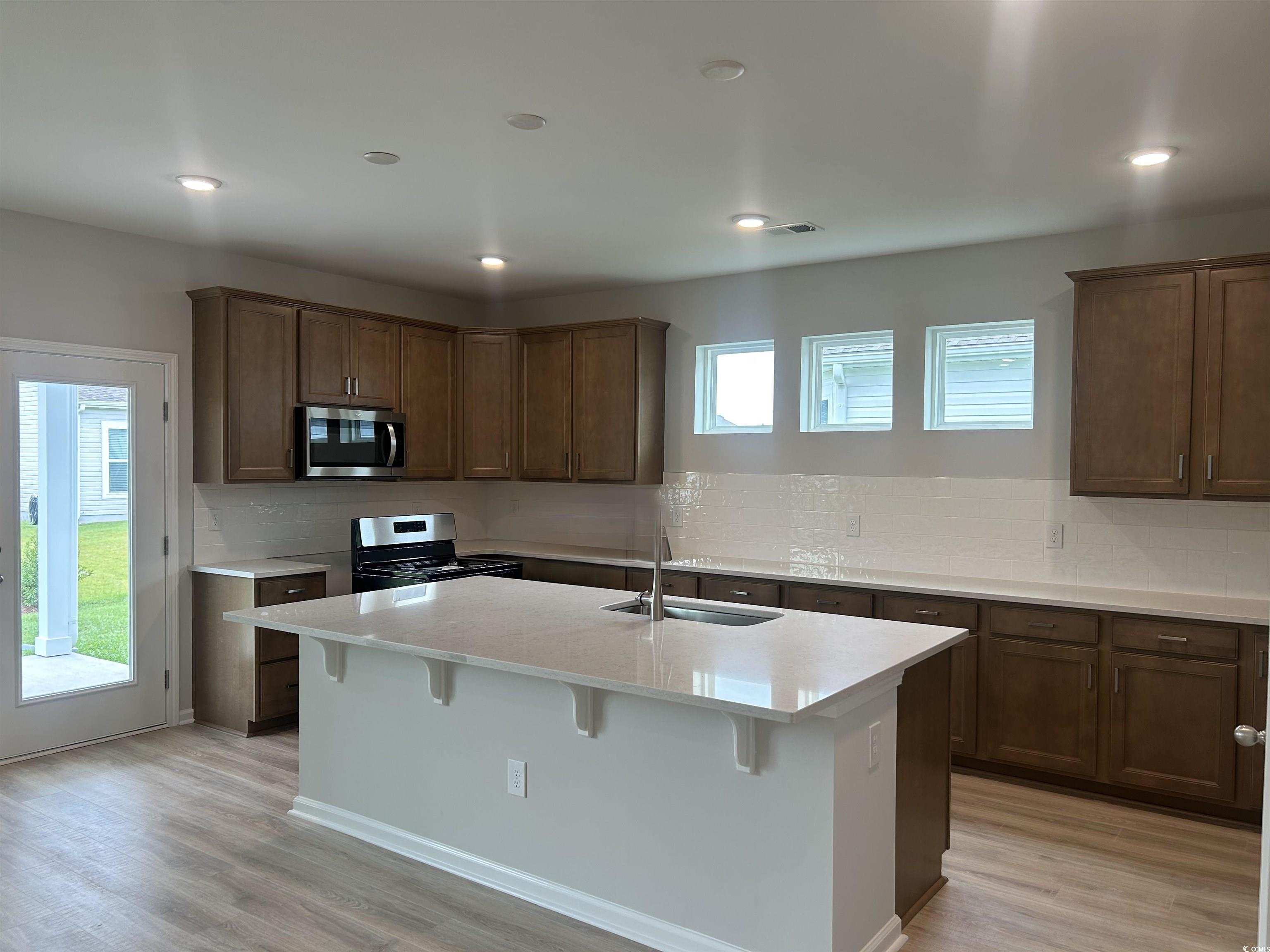 439 Kapalua Loop Little River, SC 29566 - Photo 10 of 36 Kitchen featuring backsplash, light wood-style flooring, appliances with stainless steel finishes, light countertops, and a breakfast bar area