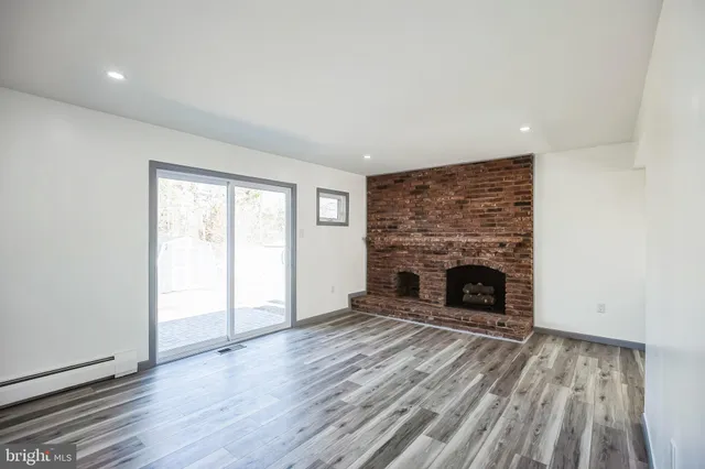 a view of an empty room with wooden floor fireplace and a window