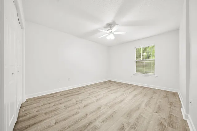 an empty room with wooden floor ceiling fan and window