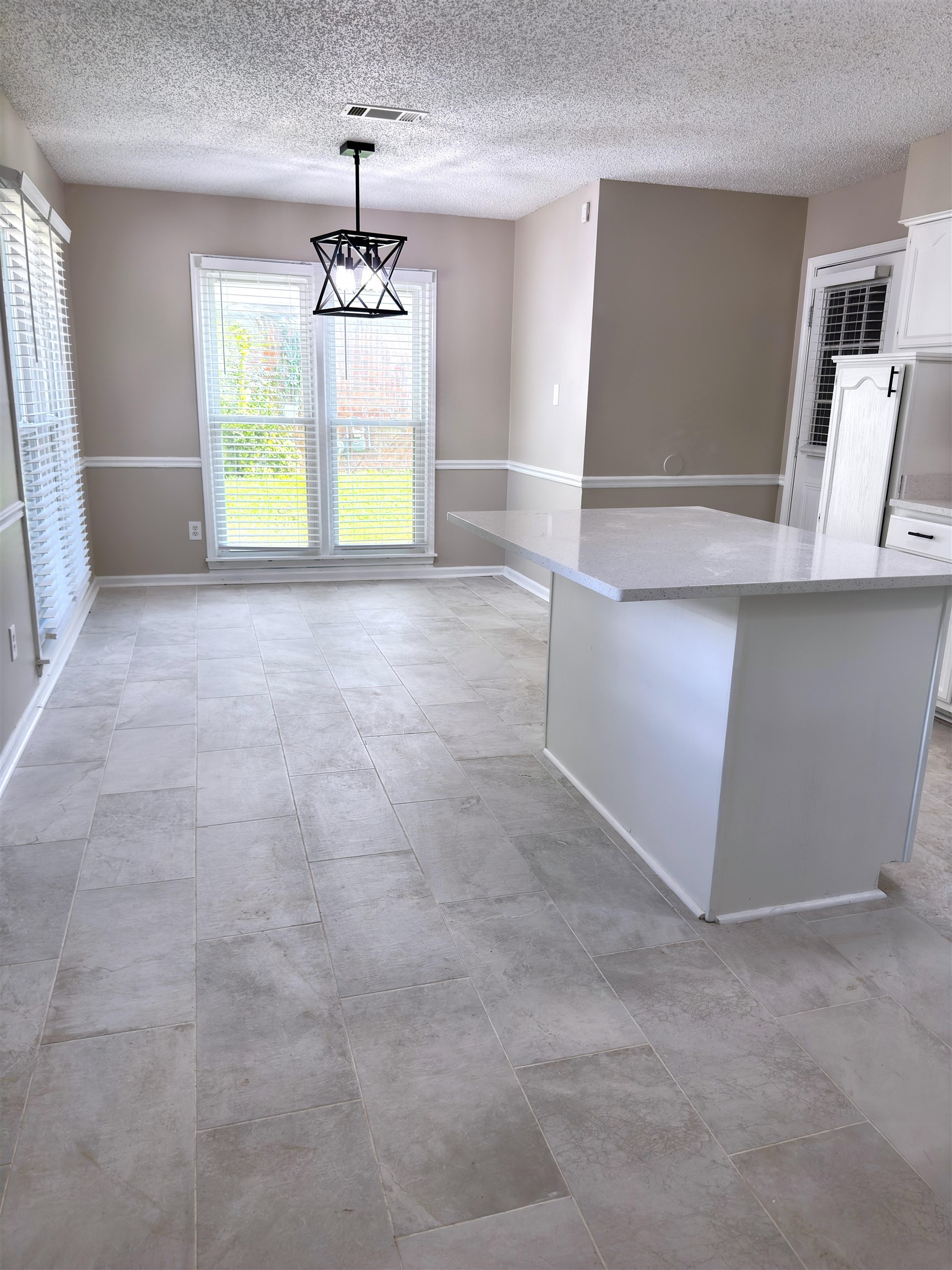 927 Cully Road Memphis, TN 38018 - Photo 7 of 33 Spacious kitchen and dining area featuring large format tile flooring, a geometric black pendant light fixture, and a kitchen island with a light-toned countertop