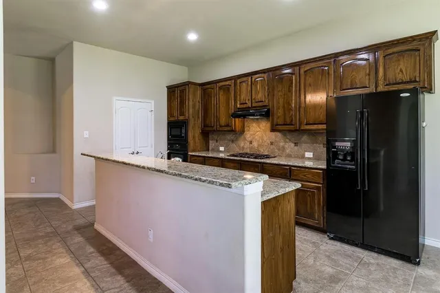 a kitchen with stainless steel appliances granite countertop a refrigerator a stove and a sink with wooden cabinets
