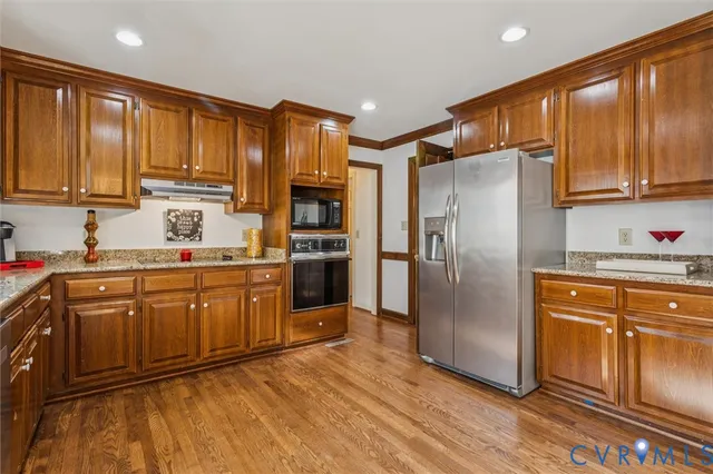 a kitchen with stainless steel appliances granite countertop a refrigerator a sink dishwasher and wooden cabinets with wooden floor