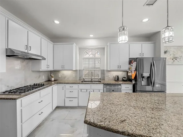 a large white kitchen with stainless steel appliances kitchen island granite countertop a stove and a refrigerator