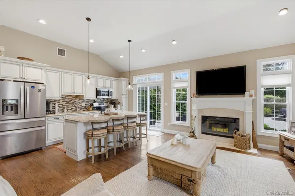 a living room with stainless steel appliances furniture a fireplace a flat screen tv and a view of kitchen