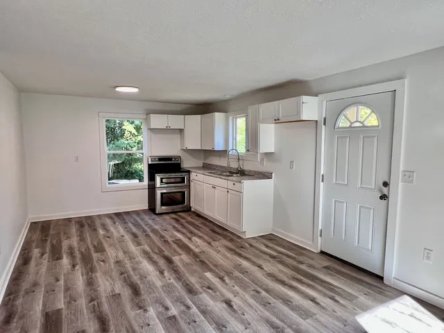 a kitchen with granite countertop a refrigerator a sink dishwasher a stove and white cabinets with wooden floor