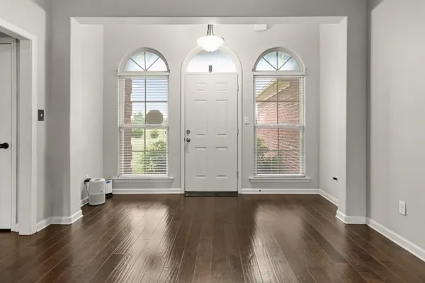 an empty room with wooden floor mirror and windows