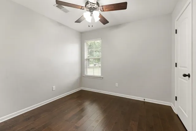 an empty room with wooden floor fan and windows
