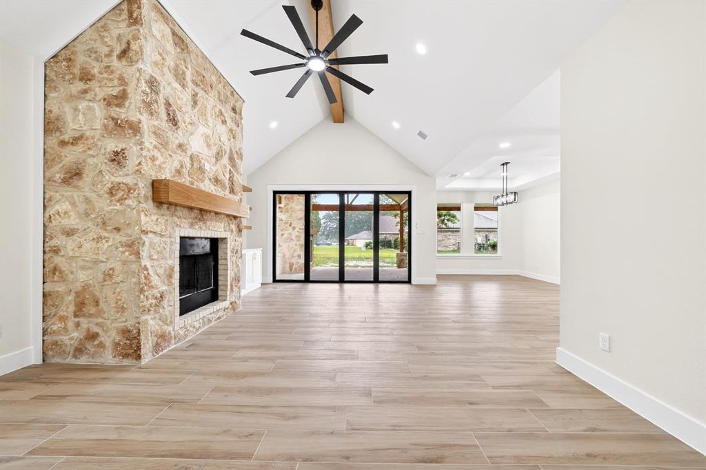 120 Springwood Road Enchanted Oaks, TX 75156 - Photo 7 of 37 Vaulted ceiling great room featuring a full-height stone fireplace with a wood mantle, wood-finish flooring, a ceiling fan, and large sliding glass doors opening to an exterior covered patio